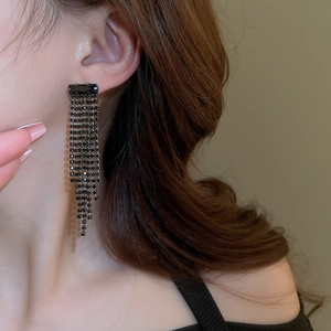 Close-up of long black rhinestone tassel earrings worn by a model in soft lighting