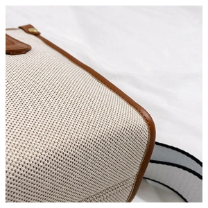 Detail of beige woven fabric tote with brown leather trim and striped strap
