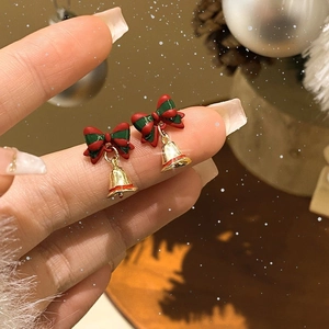 Close-up of festive red and green bow stud earrings with small golden bells on hand