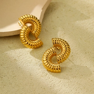 Elegante goldene gedrehte Spiralohrringe aus Titanstahl auf Steinhintergrund