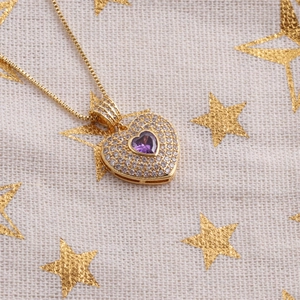 Vue macro du pendentif cœur doré avec gemme violette et zircons clairs étincelants
