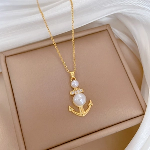 Elegante collana ad ancora dorata con perle bianche e diamanti scintillanti su sfondo seta
