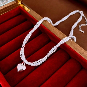 Detail of double-layer pearl necklace with a polished silver heart pendant on red velvet