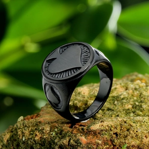 Macro shot of black stainless steel ring with spade heart engraving on red brick