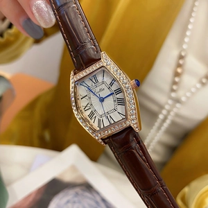 Close-up of a tonneau-shaped gold watch with diamond accents and a brown leather strap