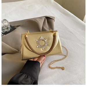 Detail of gold evening clutch bag with crystal sunburst accent and metallic chain