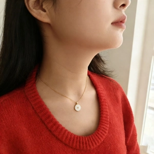 Dettaglio di una collana a catena dorata con pendente a cuore bianco indossata da una modella