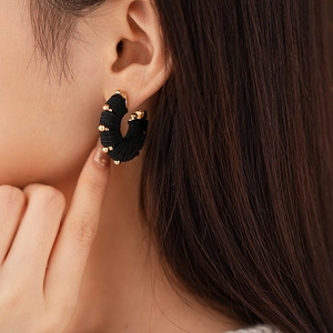 Close-up of black leather hoop earrings with gold metal beads on model's ear