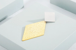 Macro shot of geometric earrings featuring a silver square post and gold textured rhombus
