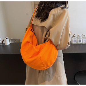 Close-up of a large bright orange nylon crescent crossbody bag worn with a khaki trench coat