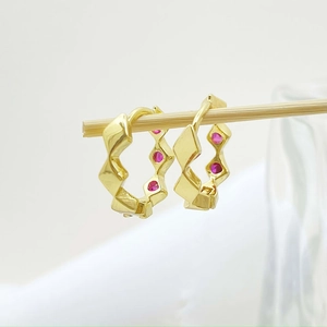 Macro shot of gold geometric hoop earrings with red round zircons on a wooden stand