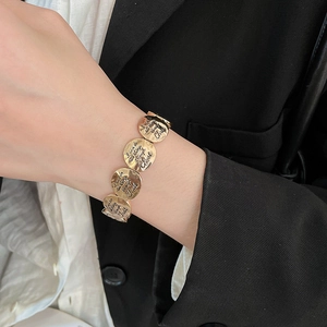 Detail of gold metal bracelet featuring engraved religious quote and hammered circular discs