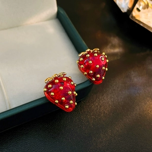 Macro shot of red resin strawberry earrings with golden leaf accents on a jewelry box