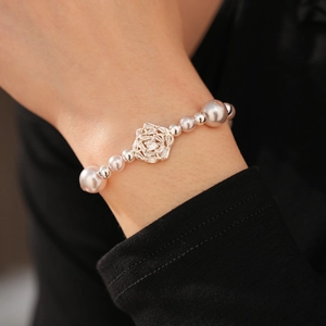 Detail of beaded pearl bracelet featuring an intricate silver rose charm with zircon inlay