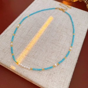 Close-up of turquoise and freshwater pearl beaded necklace with gold chain on linen pad