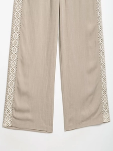 Close-up of beige wide-leg trousers featuring white lace embroidery and woven linen texture