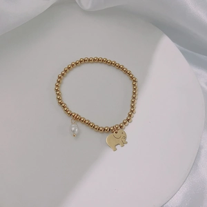 Detailed shot of gold beaded stretch bracelet with tiny elephant charm and white pearl