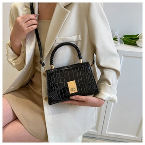 Detail of black crocodile texture handbag with gold clasp on model in beige blazer