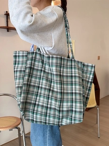 Green checkered canvas tote bag worn by a model in a cozy minimalist interior