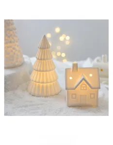 Glow ceramic Christmas tree and house decor on snow with warm LED lights and bokeh