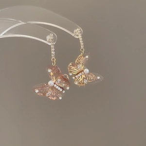 Close-up of golden butterfly earrings with transparent pink wings and pearl accents