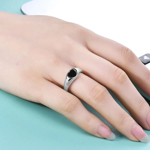 Close-up of a silver ring with a black heart inlay on a model's finger in bright setting