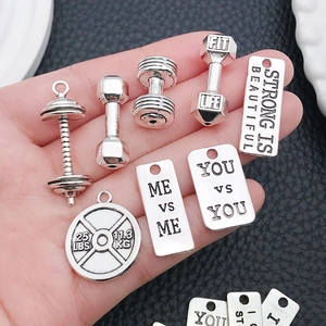 Close-up of silver fitness charms featuring dumbbells and motivational engraving in a hand