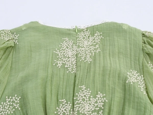 Detail view of green dress featuring white floral embroidery and back zipper closure