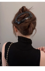 Détail d'une grande pince à cheveux ovale noire brillante fixant un chignon de mannequin