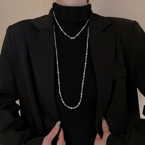 Vue détaillée d'un long collier de perles argentées porté sur un pull noir à col roulé chic