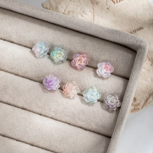 Glittery resin camellia flower stud earrings in various colors on velvet tray
