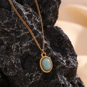 Close-up of gold stainless steel necklace with oval green natural stone on rock