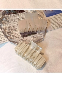 Detailed top view of beige and light grey ink pattern acetate hair claws on vintage newspaper