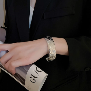 Detail of wide metallic floral embossed bangle worn with a chic black suit