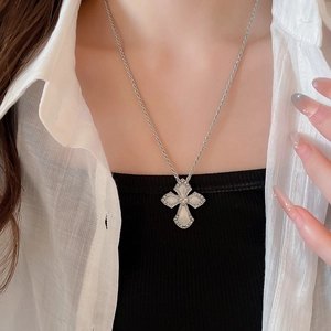 Close-up of silver cross pendant necklace with white shell inlay and heart detail on rope chain