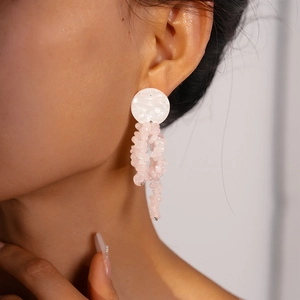 Detail of elegant earrings with white round studs and pink natural stone tassels