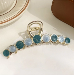 Detail of a large golden metal hair claw with blue and teal marble textured inlays