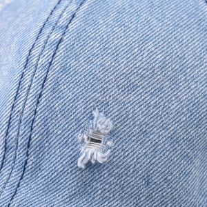 Dettaglio cappello baseball in denim azzurro con bordi sfilacciati e doppia cucitura