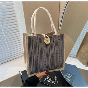 Close-up of linen tote bag with striped texture, rope handle, and wooden button detail