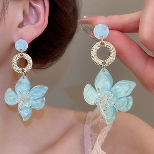 Makroaufnahme blauer Blumen-Resin-Ohrringe mit vergoldeten Details und Perlen