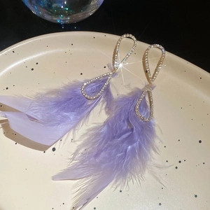 Macro shot of gold teardrop earrings with crystals and purple feather details