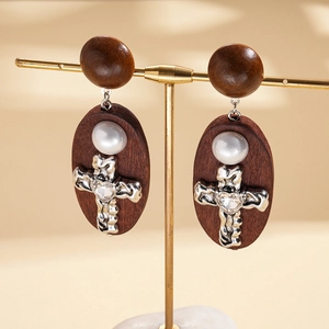 Close-up of wooden cross earrings with heart crystal and pearl on a T-bar stand