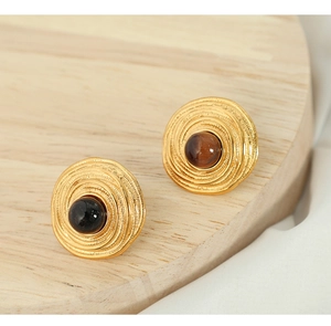 Macro shot of gold spiral earrings with tiger eye stones on white silk and wood