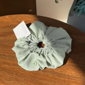 Close-up of sage green cotton scrunchie with button accents on a wooden background
