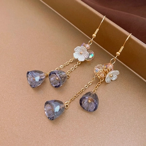 Close-up of elegant gold tassel earrings with white flower and purple crystal drops