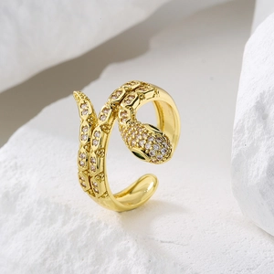 Gold snake ring with white zircons and green gemstone eyes on white stone background