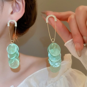 Detail showing elegant long tassel earrings with green shell-like disks and sparkling crystals