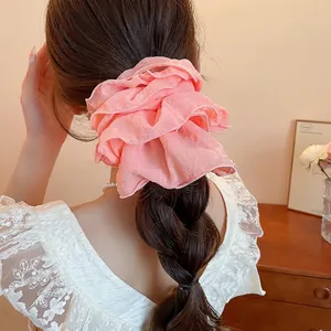 Pink ruffled fabric scrunchie with layered lace design on model's hair in warm lighting