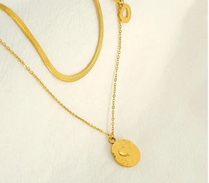 Macro shot of double-layer gold chain with heart engraved oval pendant on white fabric