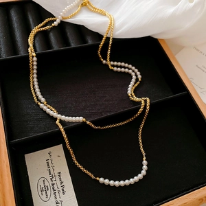 Détail d'un collier chaîne dorée et perles blanches sur un présentoir en velours noir